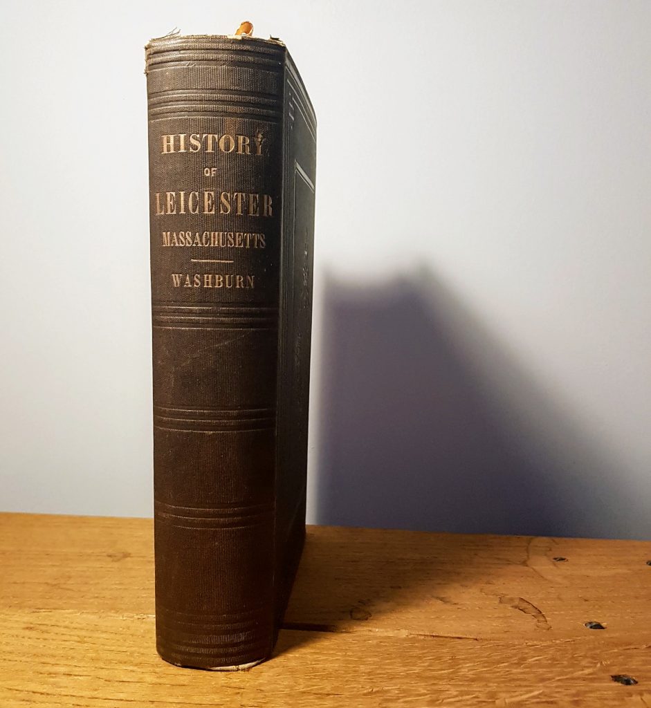 A hardback copy of History of Leicester Massachusetts by Emory Washburn, standing on a wooden table.